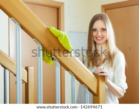 Cheerful long-haired woman cleaning wooden stair railings at home