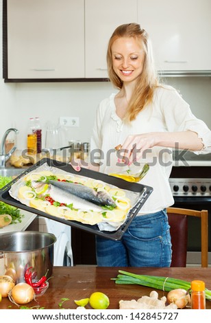 woman pouring oil into raw fish in sheet pan at home kitchen