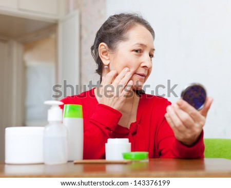 mature woman stares for facial wrinkles in mirror  at home