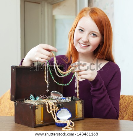 red-headed girl looks jewelry in treasure chest at home