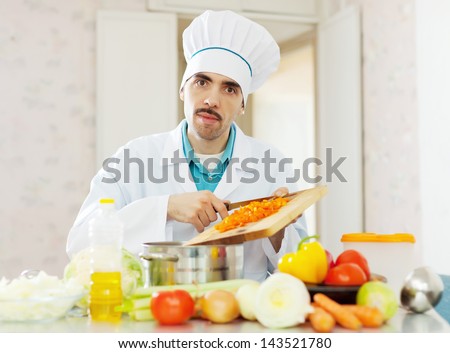 caucasian cook in uniform works with vegetables at kitchen