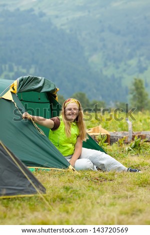 Happy female hiker in front of camp tent against mountains