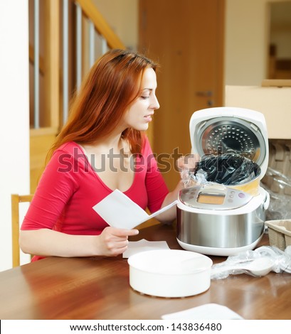 cheerful woman unpacking and reading manual for new crockpot at home interior