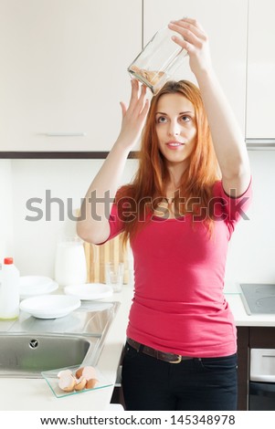 Happy woman cleaning glass bottle with egg shell in the kitchen