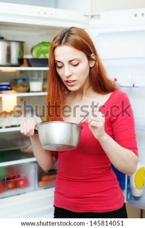 hungry girl eating from pan near fridge  at home