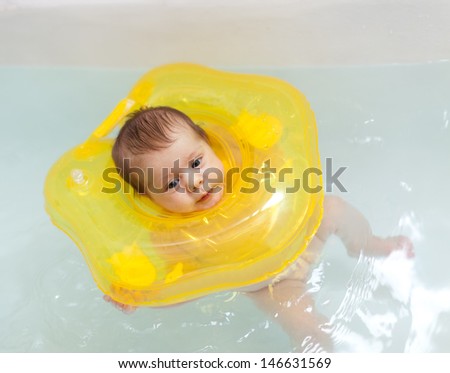 Two month baby girl swimming with neck swim ring in bath