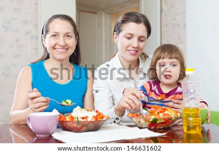 Two happy women with baby girl eats vegetables salad