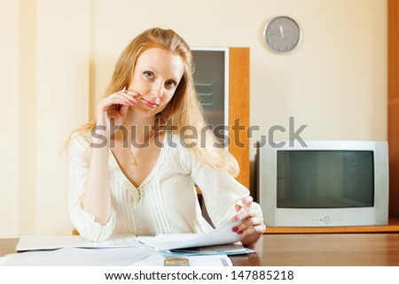 serious blonde woman looking financial documents at table in home interior