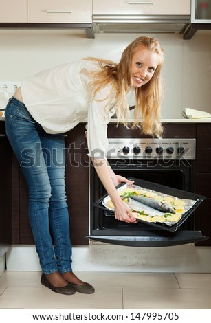 Smiling woman cooking fish in oven at home kitchen