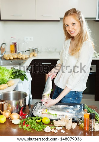 Cheeful woman cooking full fish with lemon in sheet pan at  kitchen