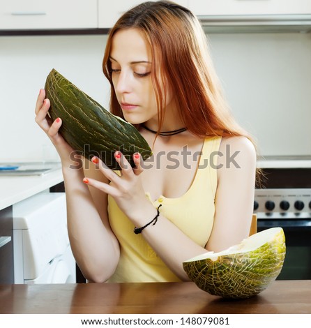 long-haired woman with ripe melon in home kitchen