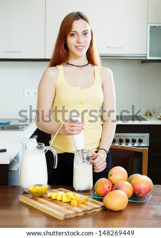 Young woman making beverages with blender from mango and milk at domestic kitchen