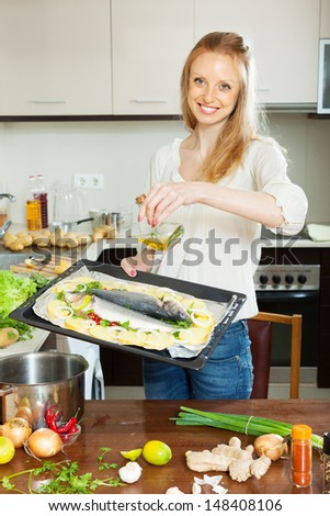 Happy woman pouring oil into fish in sheet pan at kitchen