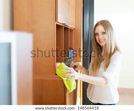 Happy blonde long-haired woman wiping the dust from furniture at home