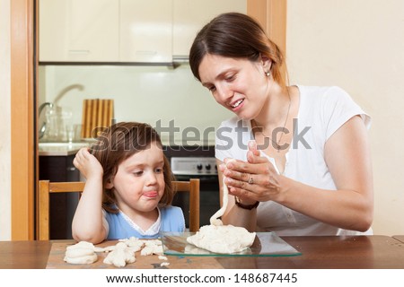 A girl with her mother learns to mold dough figurines in home interior