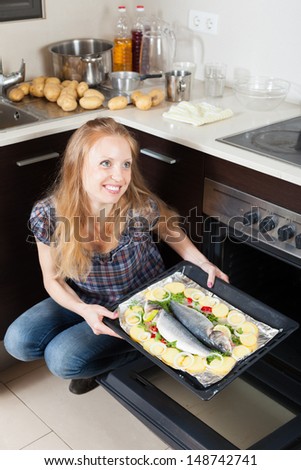Happy girl cooking raw fish in oven at kitchen