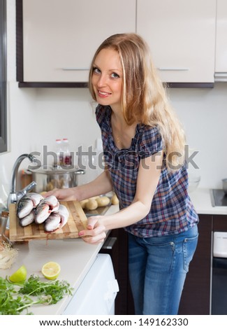 Smiling woman with raw fish in the kitchen