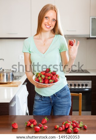 Happy blonde girl holding strawberries at home kitchen