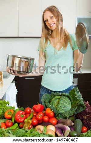 happy blonde woman with cooks pan in home kitchen