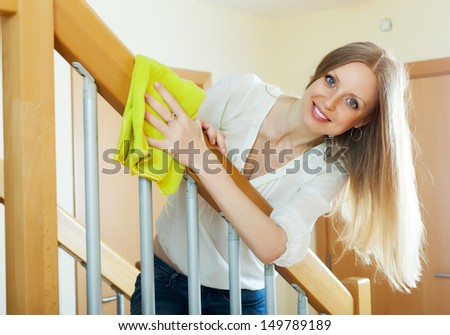 long-haired housewife cleaning stair railings with rag at home