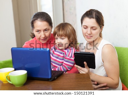 Happy family of three generations with electronic devices on sofa in living room