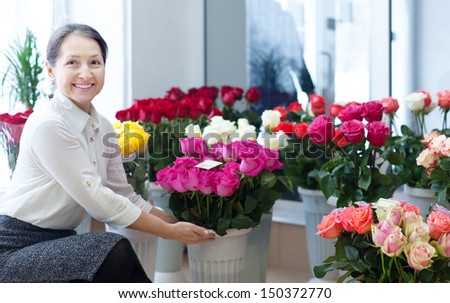 Happy mature woman chooses roses at flower store