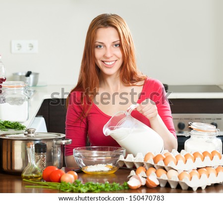 Smiling girl in red cooking omelet with milk in home kitchen