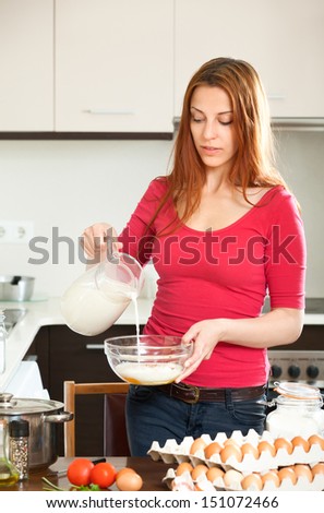 Ordinary girl in red cooking omelet with milk in home kitchen