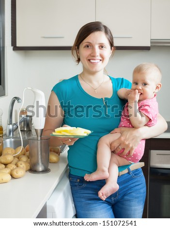 Young woman and baby girl cooking mashed potatoes with blender in kitchen