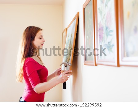 Long-Haired Girl Hanging Pictures In Frames On Wall At House
