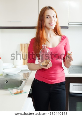 Positive woman in red cleaning glass bottle with egg shell in the kitchen