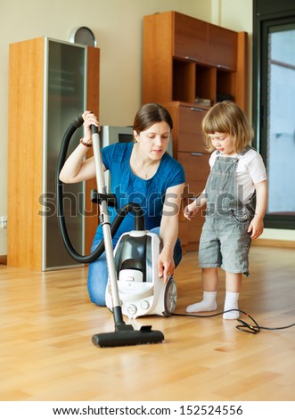Woman teaches daughter to use the vacuum cleaner in living room