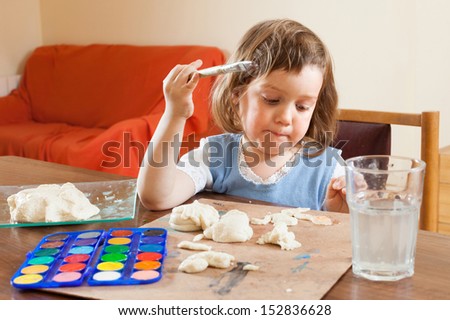 Cute little girl learning to paint dough figurines in the room