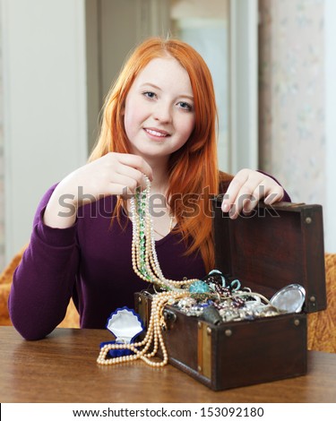 portrait of  red-headed teen girl looks jewelry in treasure chest