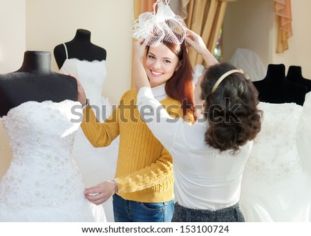 shop consultant helps girl chooses white bridal outfit at shop of wedding fashion. Focus on bride