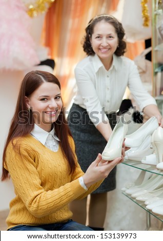 Shop assistant helps to girl chooses white shoes at shop of wedding fashion