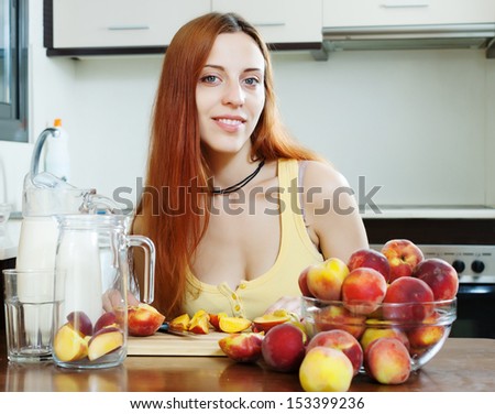 pretty long-haired woman cooking milk shake with peaches at home kitchen