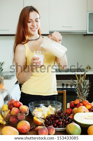 Happy woman drinking milk cocktail with fruits and milk at home kitchen