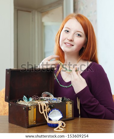 red-headed girl looks jewelry in treasure chest