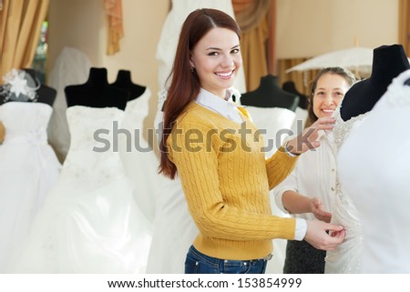 Two happy women chooses bridal outfit at  wedding boutique. Focus on young