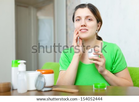 young  woman caring for her face with cosmetics at home interior