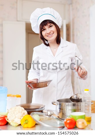 Female cook with ladle pours soup from pan in kitchen