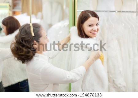 Shop assistant  helps to girl chooses fur cape  at shop of wedding fashion. Focus on young