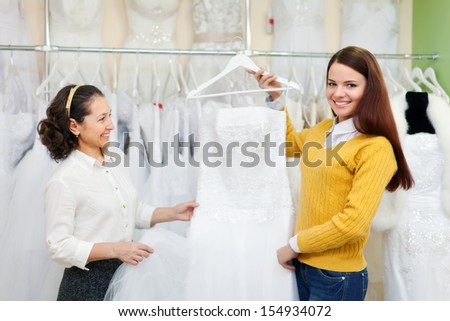 Mature woman  with daughter chooses white gown at shop of wedding fashion