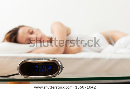 Alarm clock by the bad of sleeping woman in the morning