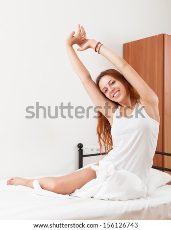 Smiling red-haired sensual girl in shirt awaking on white sheet in bed at home