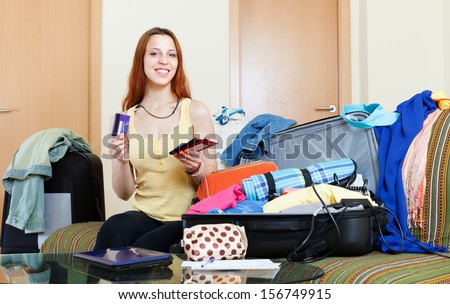 Smiling woman sitting on sofa and packing suitcase for  travel