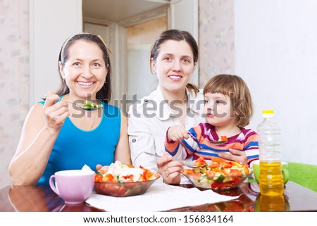 Two happy women with baby eats vegetables salad