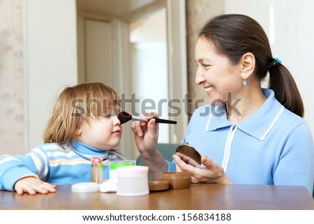 Smiling grandmother  putting facepowder on face of little girl with brush