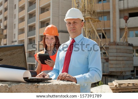 Two architects wearing protective helmet works in front of building site